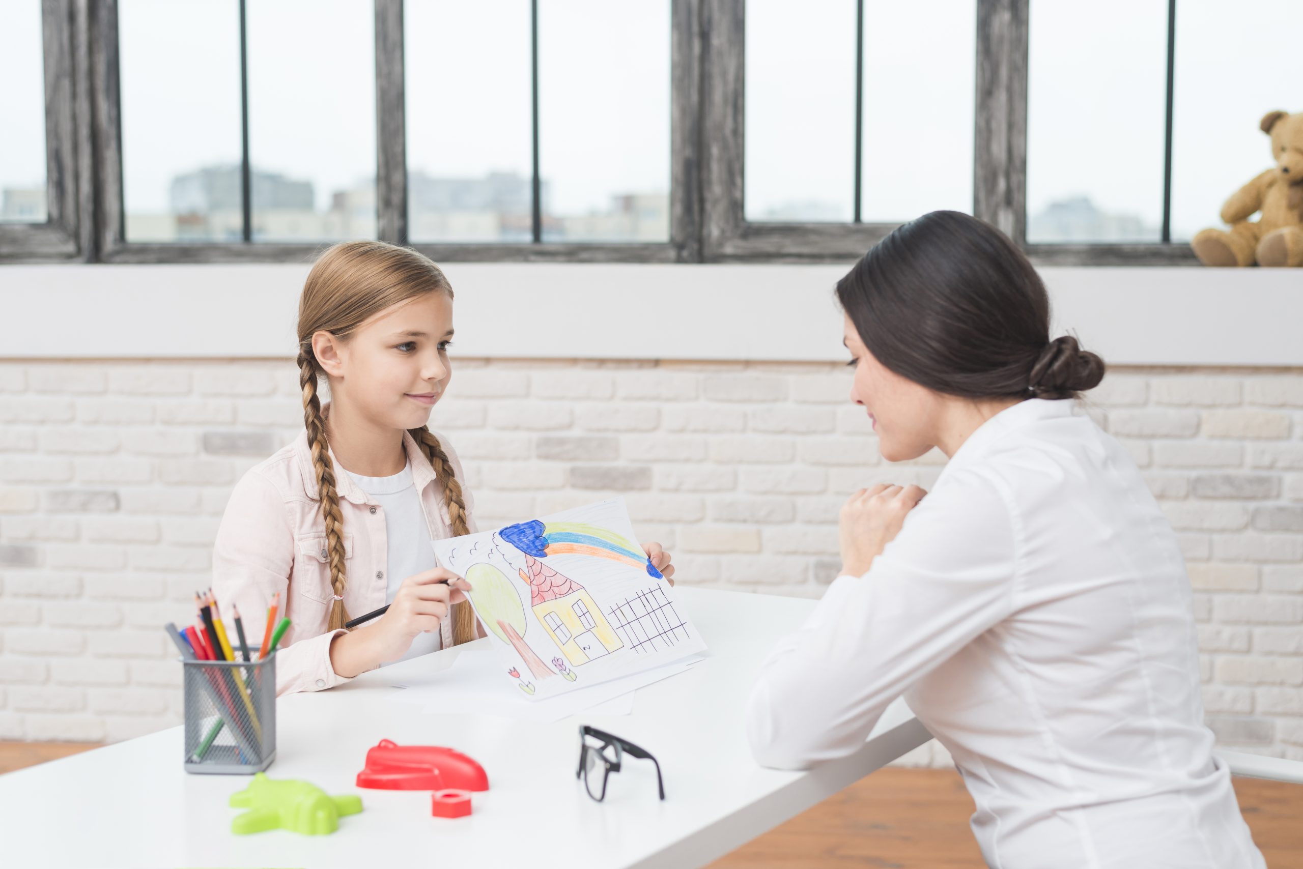 little-blonde-girl-showing-drawn-house-on-paper-to-her-female-psychologist